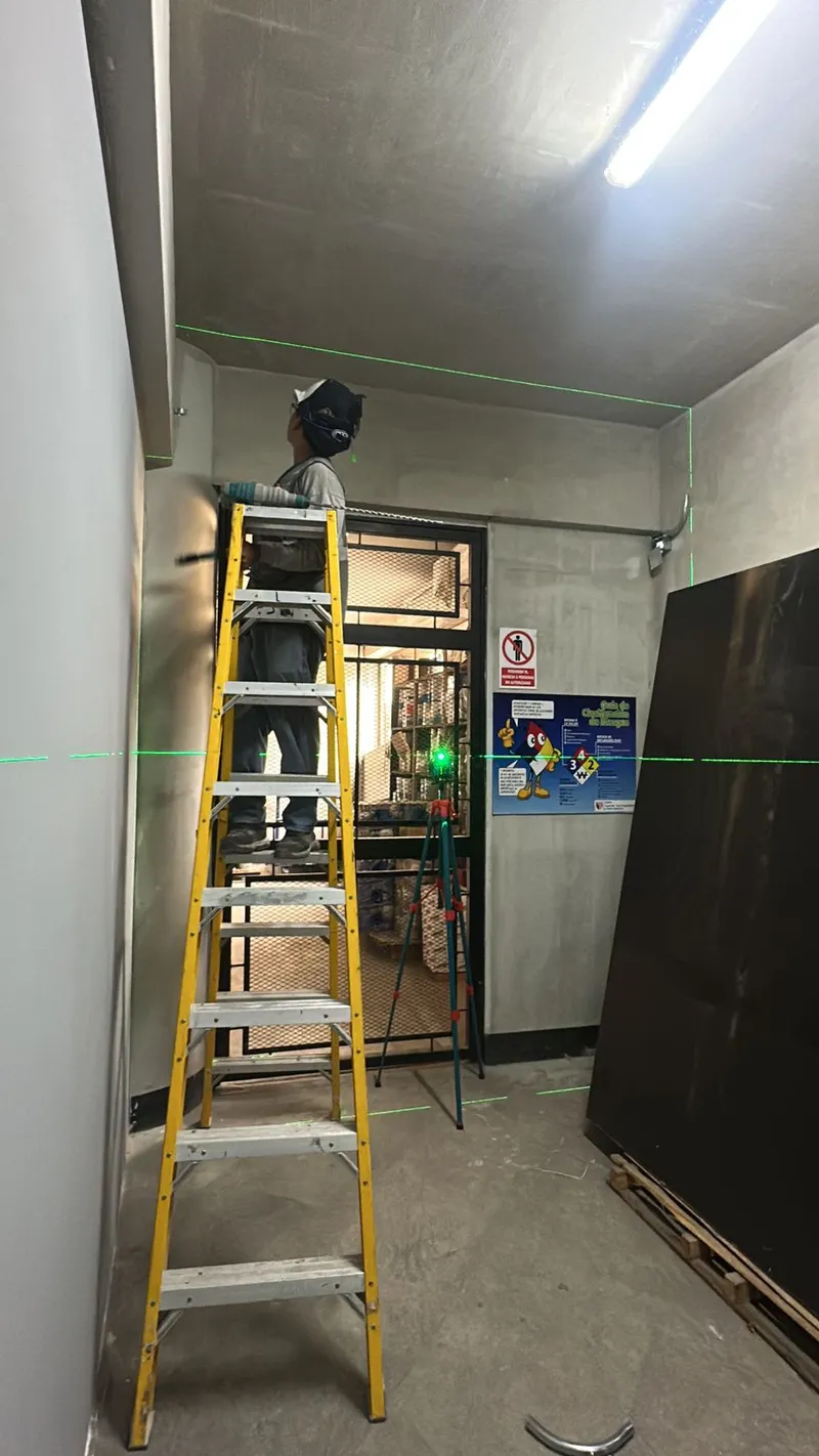 Técnico en escalera instalando sistema en interior con nivel láser verde
