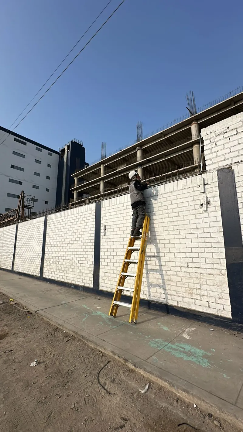 Técnico en escalera instalando cableado en muro exterior de empresa